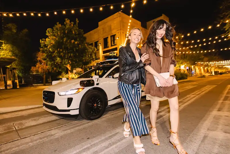 People beside a Waymo vehicle in an evening street scene